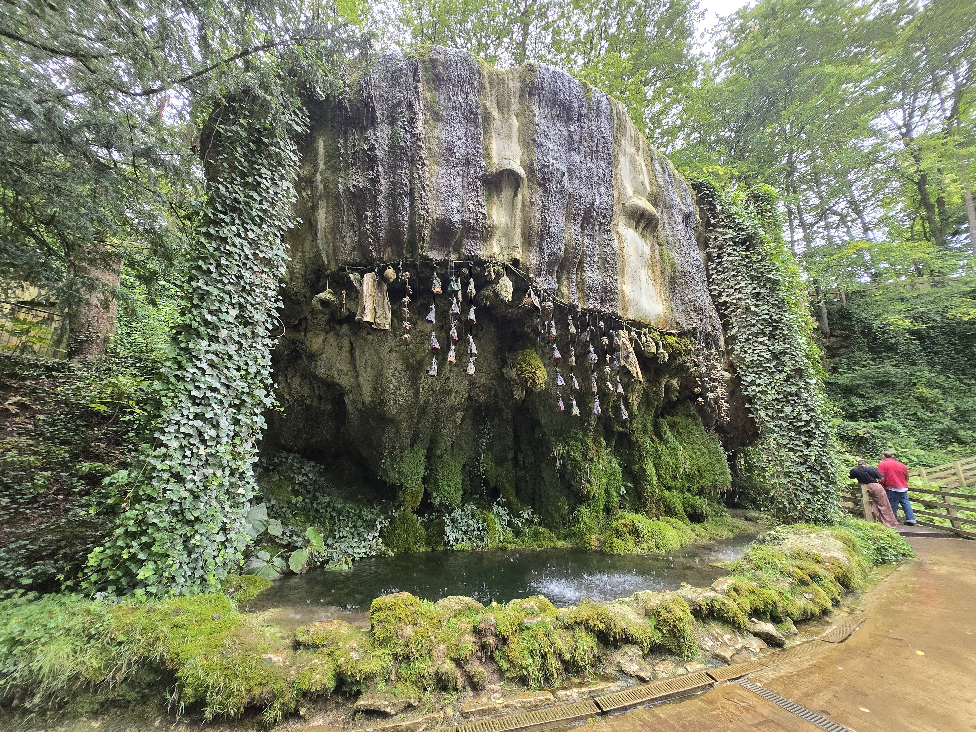 large rock with water dripping down over objects in to a pool