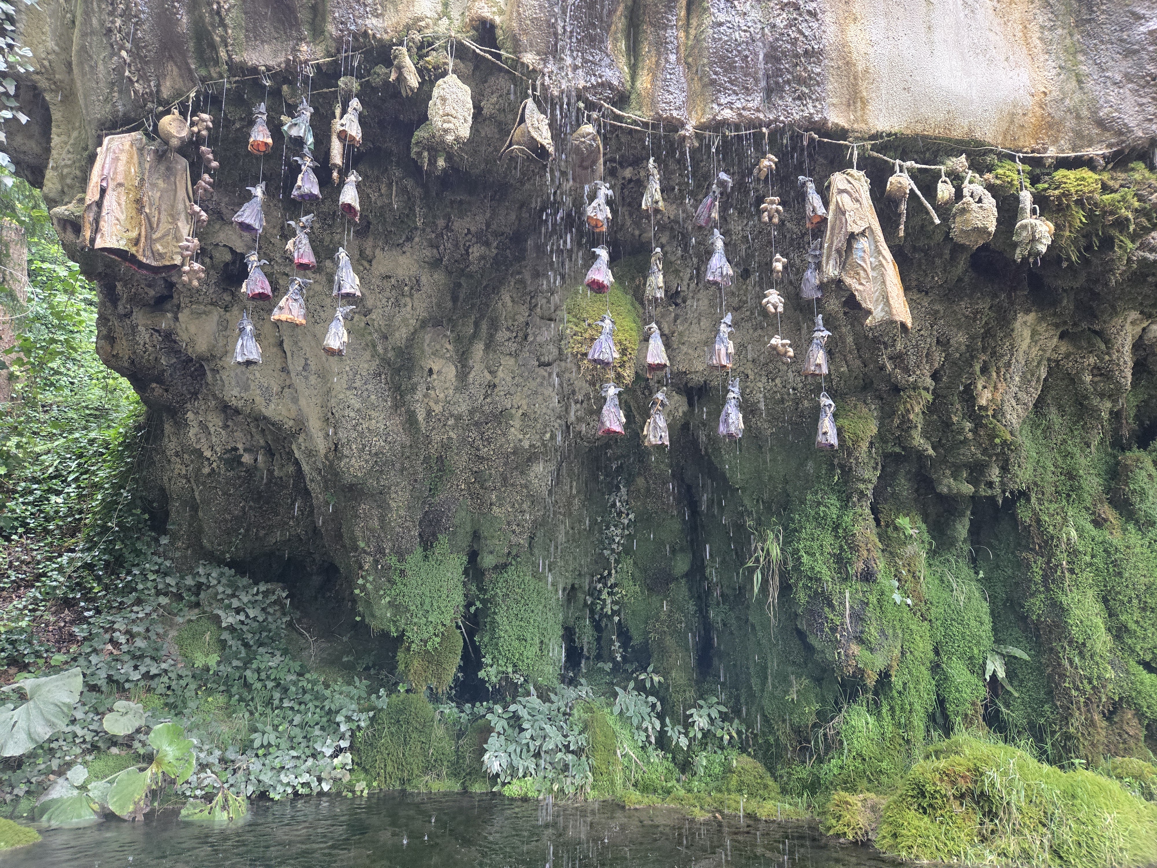 large rock with water dripping down over objects in to a pool